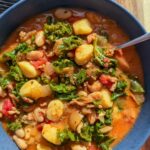 Creamy Tuscan sausage kale soup with gnocchi and white beans in a blue bowl.