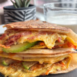 High-protein breakfast wrap filled with eggs, shredded cabbage, carrots, melted cheese, avocado, and turkey bacon, folded and crisped in a tortilla.