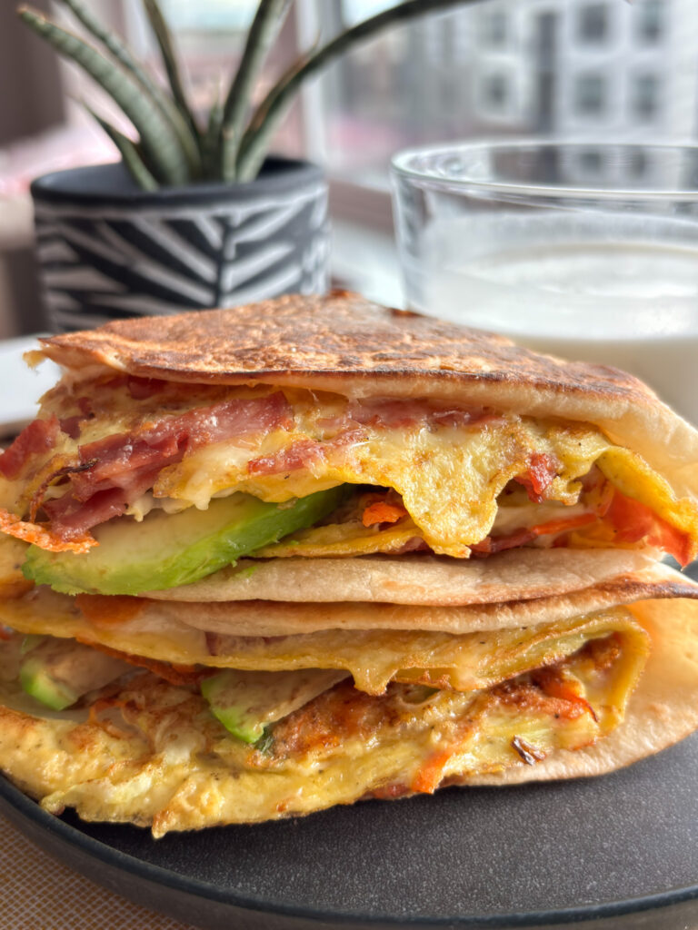 High-protein breakfast wrap filled with eggs, shredded cabbage, carrots, melted cheese, avocado, and turkey bacon, folded and crisped in a tortilla.