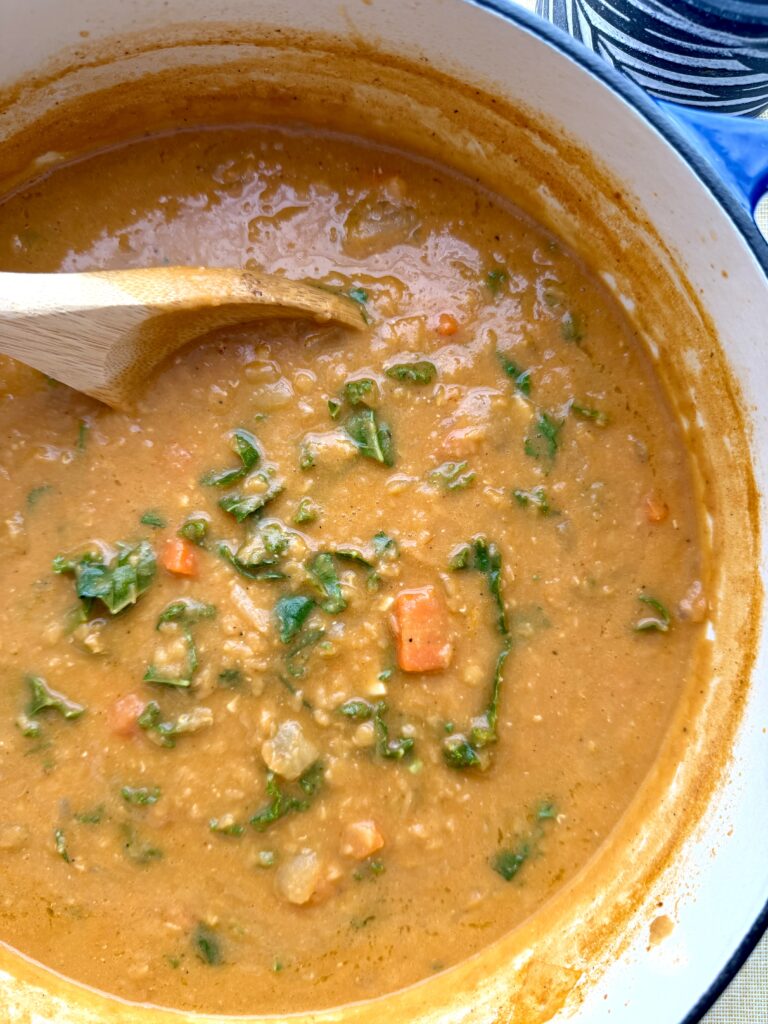 Creamy red lentil soup with kale and carrots in a white bowl, garnished with olive oil; healthy high-protein, high-fiber comfort soup